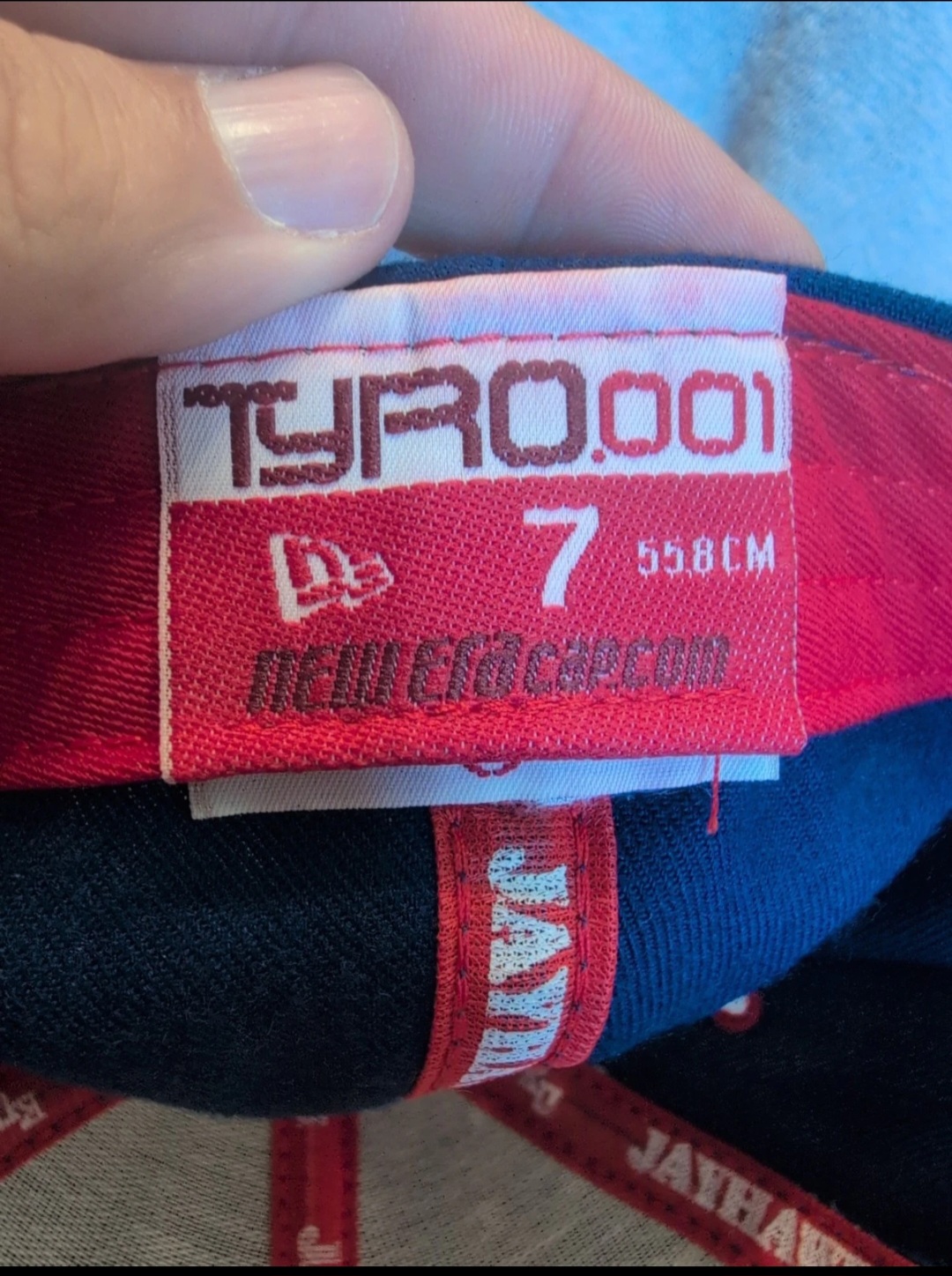 The interior sweatband tag of a New Era Tyro.001 cap, reading Tyro.001 above the New Era flag logo, size 7 (55.8 cm), and neweracap.com, with Jayhawks woven into the taping below